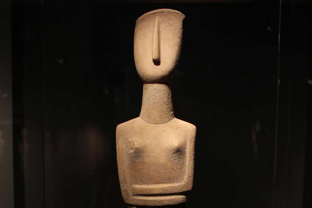 Tyypillinen naispuolinen idoli, jolla on kuvattu nenä, rinnat ja vatsan päälle päällekkäin asetetut kädet. (Kykladisen taiteen museo, Ateena)